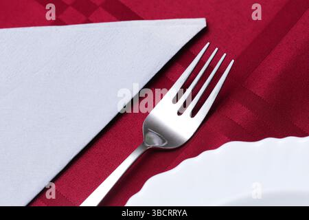 Elegant table setting closeup. Silver fork and white napkin. Red tablecloth background. Fine dining concept. Sophisticated restaurant detail. Stock Photo