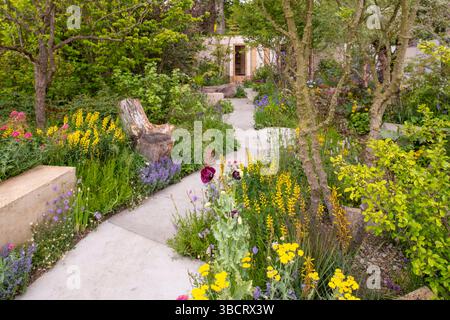 A concrete path running woodland underplanted with perennials leading to a pavilion in the Avanande Intelligent Garden Stock Photo