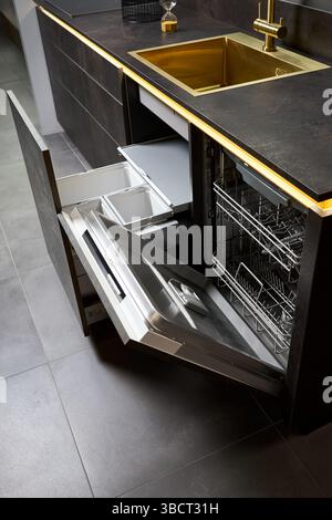 Dishwasher and kitchen waste bin cabinet. Pull out kitchen drawers for waste bin separate waste collection and Dishwasher under golden sink basin and Stock Photo