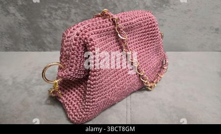 Pink women's handbag, hand knitted, with a long handle. Details and elements. On a gray background. Stock Photo
