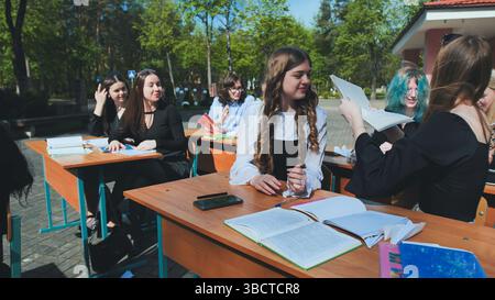 Students from high school and university are collaborating outdoors, exchanging notes and appreciating the outdoors Stock Photo