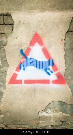 Tbilisi, Georgia – March 2024: Street art with a blue cat stencil inside a red triangle on an old textured wall in Tbilisi, Georgia. Urban graffiti sy Stock Photo