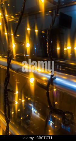 Close-up of glowing yellow LED string lights with reflections and bokeh in a night setting. Warm festive atmosphere with abstract composition and soft Stock Photo