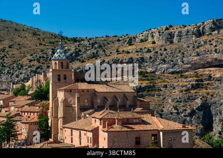 The cathedral’s tiled tower rises above terracotta buildings and rugged cliffs under a clear blue sky. Stock Photo