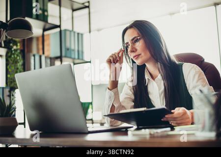 Experienced businesswoman working in an elegant office setting, wearing formal attire and analyzing data on her laptop Stock Photo