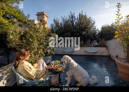Relaxed lunch on a sunny terrace in Southern Italy with a big white dog. Perfect for promoting Mediterranean lifestyle, pet-friendly travel, or outdoor dining concepts Stock Photo
