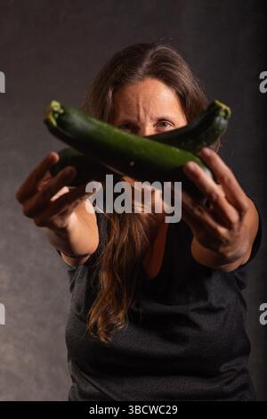 woman holding two fresh natural zucchini cut across each other in front of her face Stock Photo