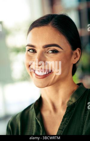 Smiling young businesswoman in a green blouse posing confidently in a modern workspace with bright natural lighting Stock Photo