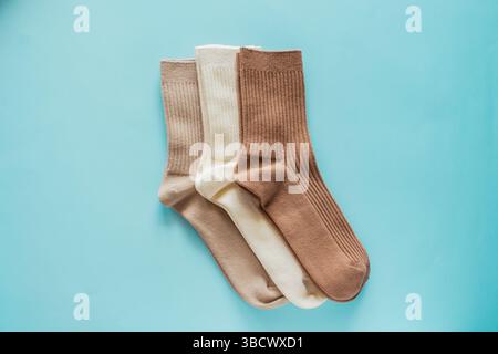 Three pairs of cozy socks in beige colors arranged neatly on soft blue background, showcasing texture and design for fashion and comfort enthusiasts. Stock Photo