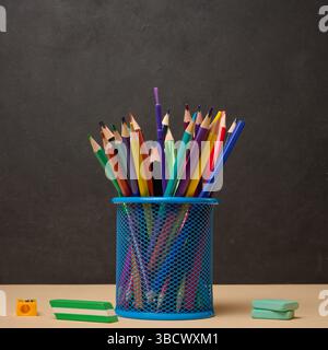 Multi-colored pencils in a blue metal cup, sharpener and erasers symbolizing study or creativity Stock Photo