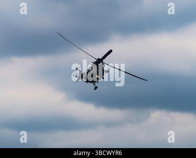 Side View of a Military Helicopter in Flight Against a Turquoise Sky, Capturing the Details of the Aircraft's Profile and Creating a Dynamic Aviation Scene. Stock photograph Stock Photo