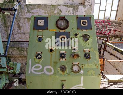 Amlwch, North Wales, UK, 05-17-2025: A rusty control panel stands in an abandoned industrial setting, featuring faded paint and graffiti.Highlighting Stock Photo