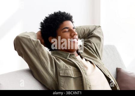 Happy black teen guy relaxing on comfortable sofa at home during coronavirus quarantine Stock Photo