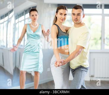 Couple practicing passionate tango guided by female dance instructor in studio Stock Photo