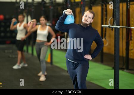 Bearded man doing kettlebell overhead shoulder press in gym Stock Photo