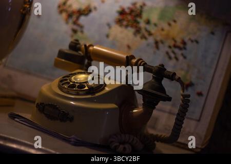 Close-up of a vintage rotary telephone with an antique design, set against a blurred world map background, evoking nostalgia and travel themes Stock Photo