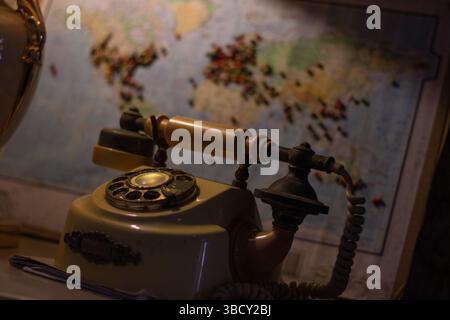 Close-up of a vintage rotary telephone with an antique design, set against a blurred world map background, evoking nostalgia and travel themes Stock Photo