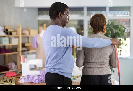 Male tailor using measuring tape to measure clothes on woman in sewing studio Stock Photo