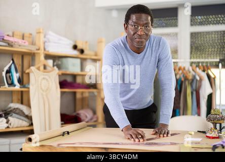 Male tailor draws sketch of future clothing on paper using patterns in sewing workshop Stock Photo