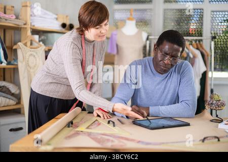 Two sewing workshop workers draw patterns on electronic tablet Stock Photo