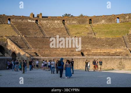 Tourists within the amphitheatre of Pompeii in Italy. Pompeii was a Roman town in the Bay of Naples with a population of around 20,000 that was destroyed when the volcano Mount Vesuvius erupted in 79 CE. The eruption buried the town under a thick layer of ash, which preserved the site, allowing archaeologists to glean much about life in the Roman Empire. Stock Photo