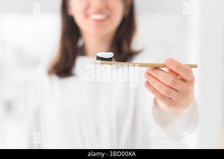 Woman with applied paste on bamboo tooth brush in bathroom, closeup Stock Photo