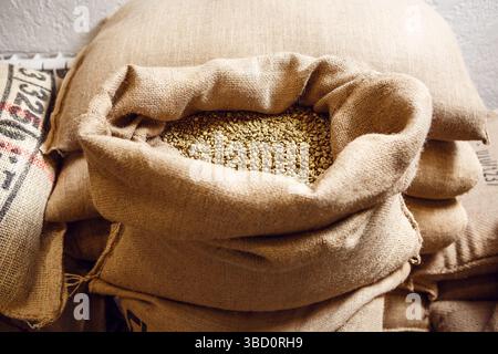 Open Coffee Bag Revealing Contents Among Stacked Bags in a Warehouse, Emphasizing Storage and Handling Process of Coffee Beans Stock Photo
