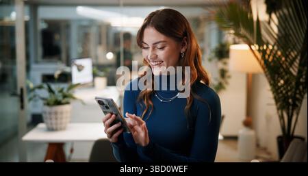 Cellphone, business and happy woman in office at night for communication, contact or funny email. Female employee, tech and scroll for feedback Stock Photo