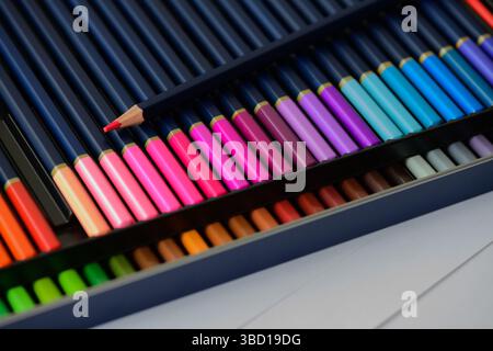 Two rows of colored pencils with a sharp point on red pencil in pencil case, Big beautiful color palette watercolor pencils for creativity drawing. Stock Photo