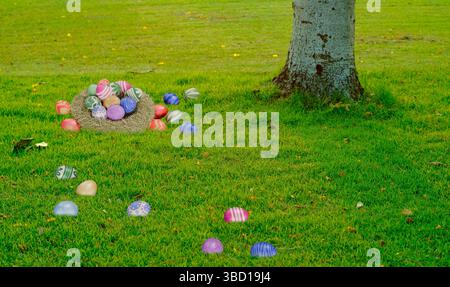 A nest of colorful Easter eggs on grass with eggs scattered around a tree. Perfect for Easter, spring celebrations, and festive holiday themes Stock Photo