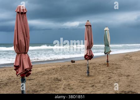 Three umbrellas are on the beach. The sky is cloudy and the ocean is in the background Stock Photo