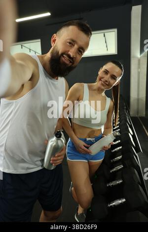Couple with water bottles taking selfie after training in gym Stock Photo