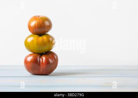 Three bright ripe juicy tomatoes in red and yellow on a blue wooden table, side view. Healthy food, fresh healthy vegetables from the garden Stock Photo