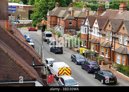 A mechanic seen from behind on a metal ladder as he checks and prepares the connection of a new customer's fiber optic cables. Dorking, UK, 2025 Stock Photo