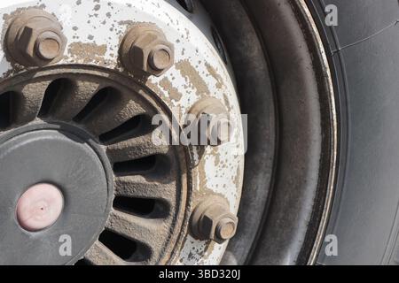Old dirty truck wheel. Close-up of rusty bolts. Heavy vehicle tire detail. Industrial machinery maintenance. Grime on metal surface. Stock Photo