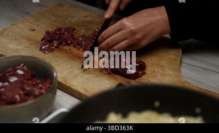 Chef Cutting Raw Chicken Liver on Wooden Board. Stock Photo