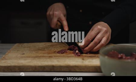 Chef Cutting Raw Chicken Liver on Wooden Board. Stock Photo