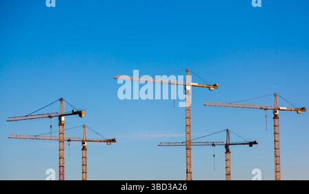 Tall tower cranes stand against the blue sky. Stock Photo