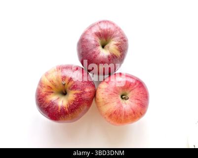 Three apples are sitting on a white surface. The apples are red and shiny. They are arranged in a triangular shape Stock Photo