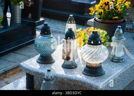Peaceful cemetery scene with glass lanterns and vibrant flowers on a granite tombstone illuminated by sunlight. Stock Photo