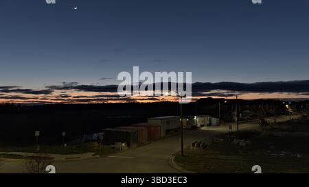 A beautiful night sky with a bright moon and a few clouds. The sky is dark and the street is lit up Stock Photo