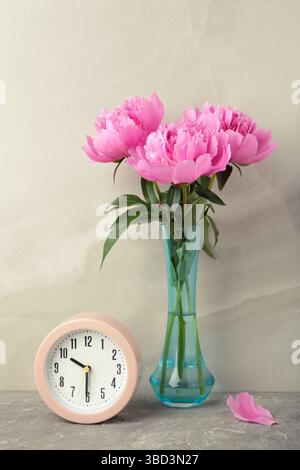 Romantic background with alarm clock and pink peonies on grey background. Vertical photo. Top view Stock Photo