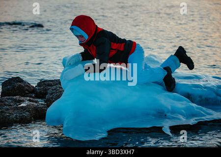 Young woman tourist climbs on ice trying not to fall in water, danger and survival concept Stock Photo