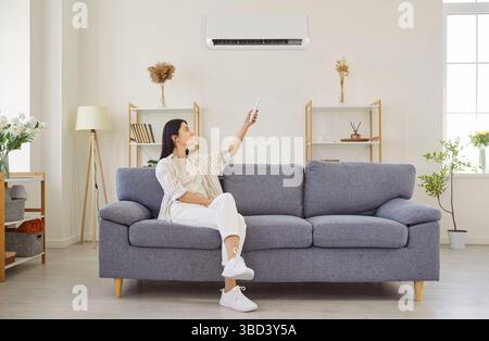 Woman switching on air conditioner at home, blowing warm, cold air room temperature control Stock Photo