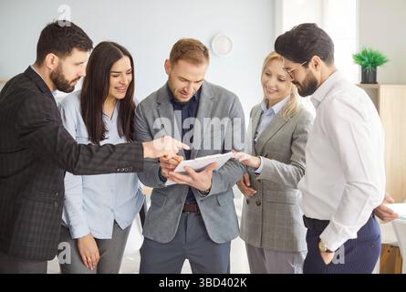 Business group discussing project details, diverse colleagues meet in office, standing share opinion Stock Photo