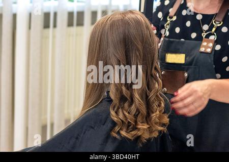 Professional hairstylist creating stylish curls on young girl's long hair Stock Photo