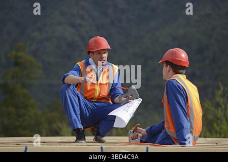 GREYMOUTH, NEW ZEALAND, AUGUST 5, 2015: Two electricians discuss the plan for a major construction job while sitting on the rafters of a new building Stock Photo