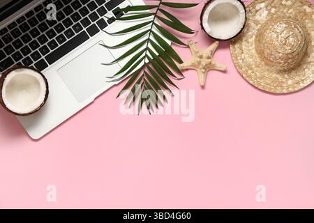 Laptop with palm leaf, hat and coconut on pink background Stock Photo