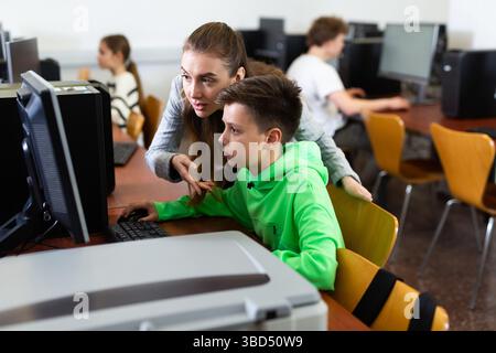 Female teacher consulting tween boy studying in computer class Stock Photo