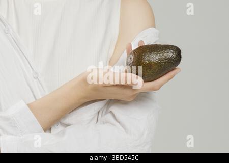 Unrecognizable woman holds avocado in hand Stock Photo